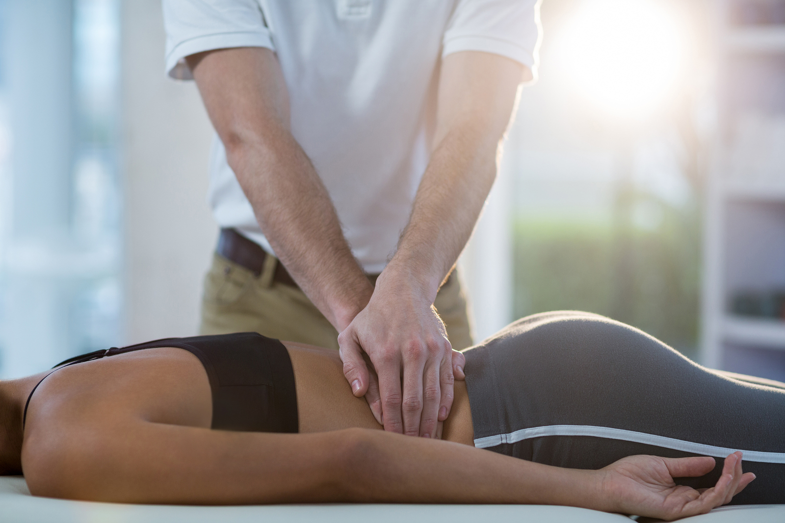 Male physiotherapist giving back massage to female patient in cl