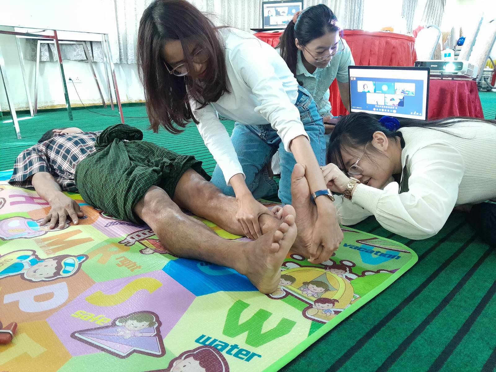 Physiotherapist in Burma practicing treatment techniques with a volunteer patient during ReLAB-HS Clinical Skills Training session facilitated online by International mentor Stacy Schiurrring