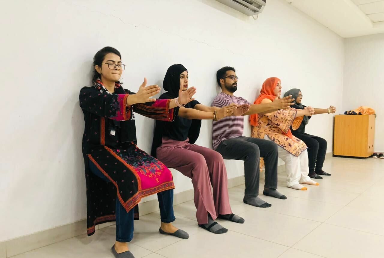 Image shows 5 participants of an exercise class in Pakistan doing a wall squat as a result of a new programme following clinical skills training using the online learning Physical Activity Programme on Physiopedia Plus online learning for physiotherapists, physical therapists and rehabilitation professionals